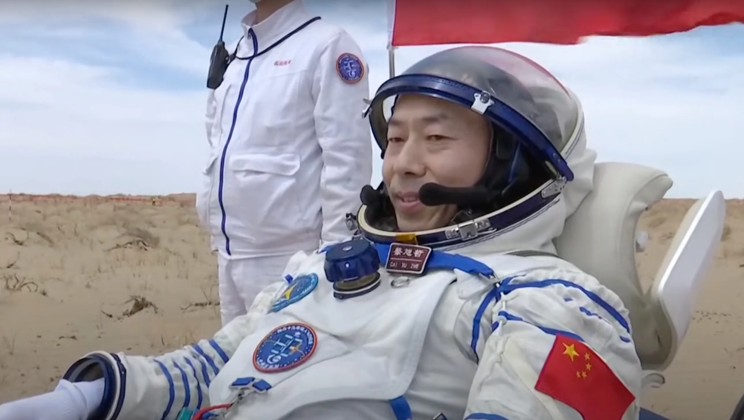 ein Astronaut in einem weißen Raumanzug sitzt kurz nach der Landung auf einem Stuhl in einer Wüstenlandschaft